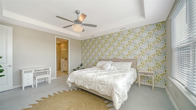 bedroom with connected bathroom, light colored carpet, ceiling fan, and a tray ceiling