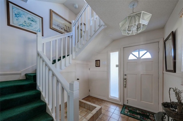 tiled entryway featuring a notable chandelier, vaulted ceiling, and a textured ceiling