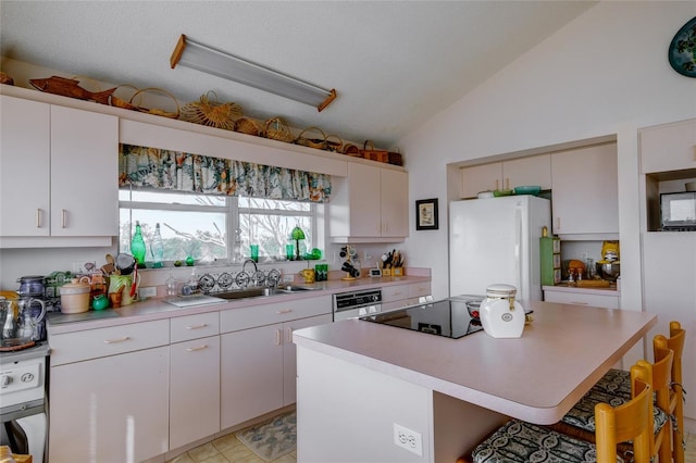 kitchen with sink, a breakfast bar area, white cabinetry, a kitchen island, and white fridge