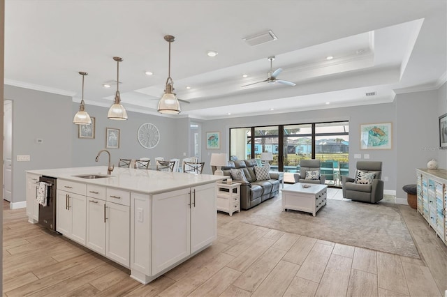 kitchen featuring pendant lighting, white cabinetry, a kitchen island with sink, a raised ceiling, and light hardwood / wood-style flooring