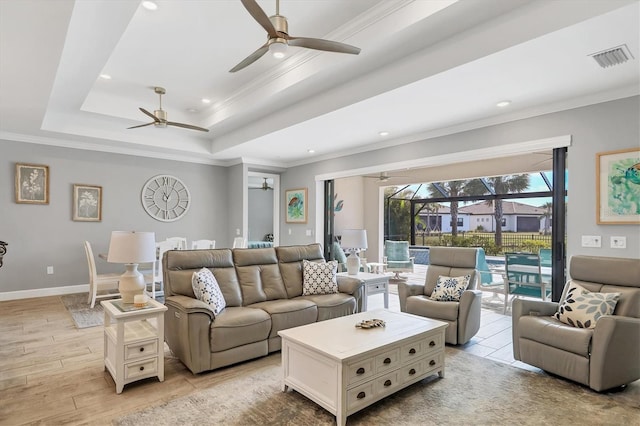 living room featuring a tray ceiling, ornamental molding, ceiling fan, and light wood-type flooring