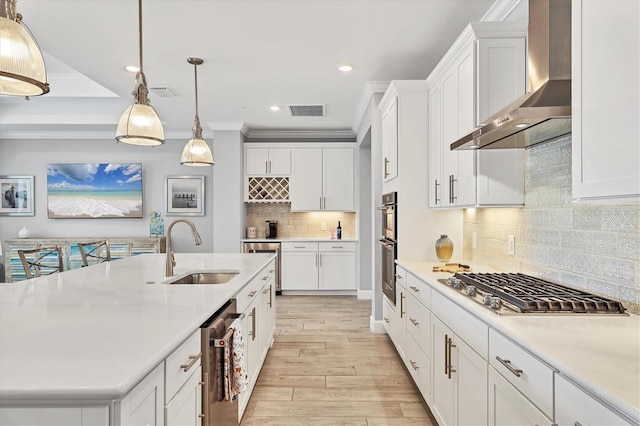 kitchen with sink, white cabinetry, hanging light fixtures, a kitchen island with sink, and wall chimney range hood