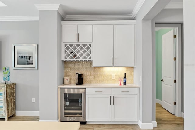 bar with white cabinetry, tasteful backsplash, ornamental molding, beverage cooler, and light wood-type flooring