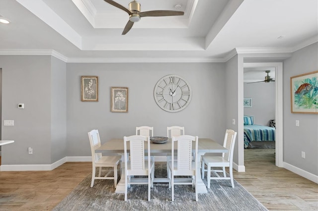 dining room with a raised ceiling, crown molding, and light hardwood / wood-style flooring