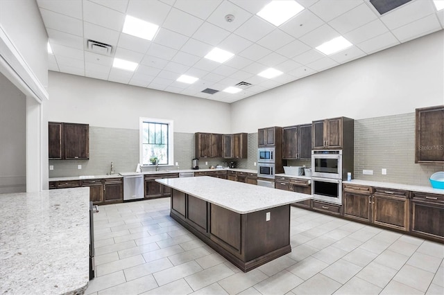 kitchen with dark brown cabinetry, a center island, a high ceiling, decorative backsplash, and a drop ceiling