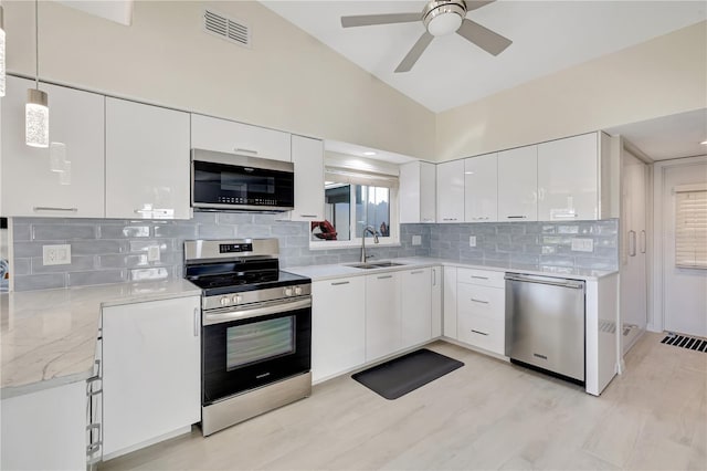 kitchen with appliances with stainless steel finishes, pendant lighting, lofted ceiling, sink, and white cabinets