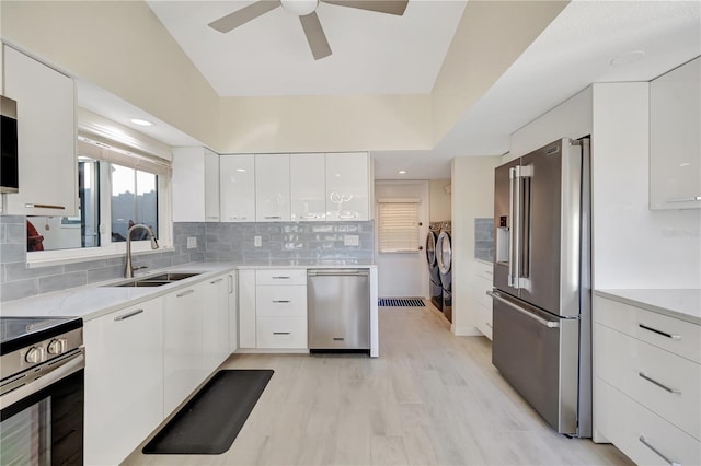 kitchen with sink, washer and clothes dryer, white cabinetry, stainless steel appliances, and tasteful backsplash