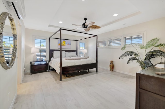 bedroom featuring ceiling fan, a wall mounted AC, light hardwood / wood-style floors, and a tray ceiling