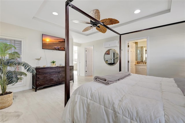 bedroom with ceiling fan, a wall unit AC, ensuite bathroom, light hardwood / wood-style floors, and a raised ceiling