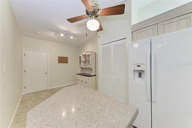 kitchen with ceiling fan, white fridge with ice dispenser, light tile patterned floors, and light stone counters