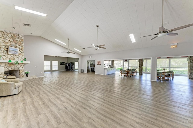 interior space featuring a stone fireplace, light hardwood / wood-style flooring, ceiling fan, and a towering ceiling