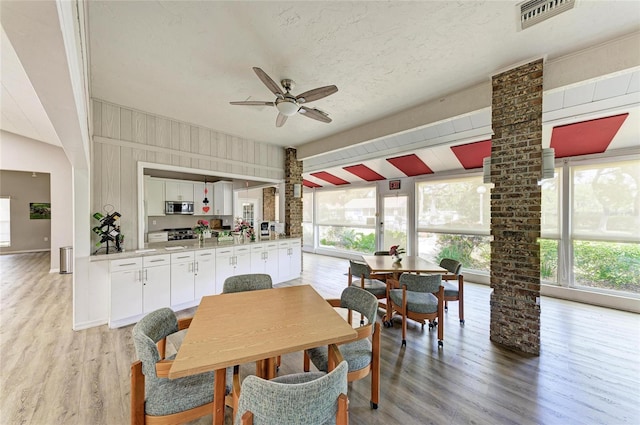 dining room with ceiling fan, wooden walls, a textured ceiling, and light hardwood / wood-style flooring