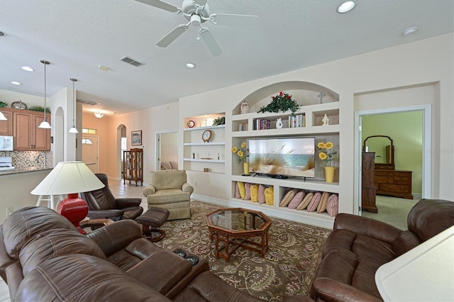 living area with built in shelves, visible vents, arched walkways, ceiling fan, and a textured ceiling