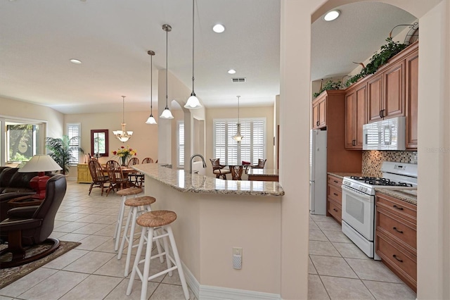 kitchen with light tile patterned floors, white appliances, tasteful backsplash, light stone countertops, and decorative light fixtures