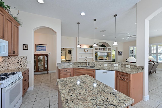 kitchen with sink, light stone counters, kitchen peninsula, pendant lighting, and white appliances