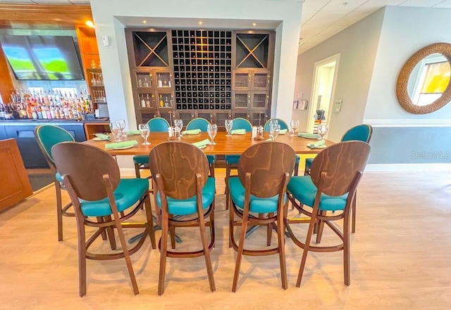 dining room featuring a dry bar, light wood-style flooring, baseboards, and a paneled ceiling