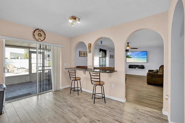 kitchen with a breakfast bar, kitchen peninsula, a textured ceiling, and light wood-type flooring