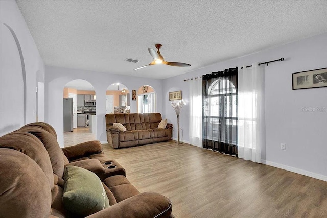 living room with ceiling fan, light hardwood / wood-style floors, and a textured ceiling