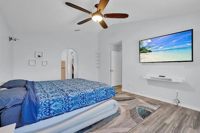 bedroom featuring a textured ceiling, vaulted ceiling, ceiling fan, and light wood-type flooring