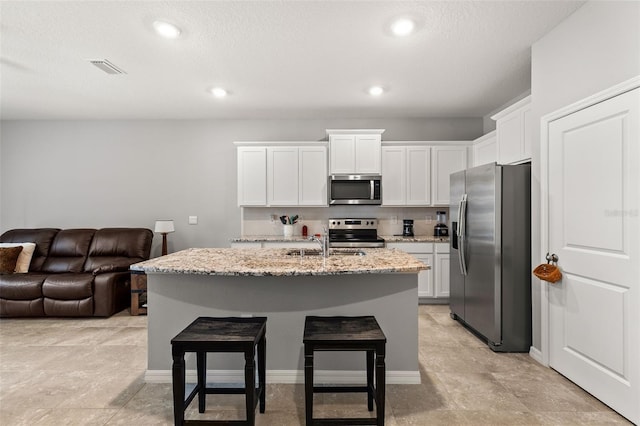 kitchen with white cabinetry, light stone counters, a kitchen island with sink, and appliances with stainless steel finishes