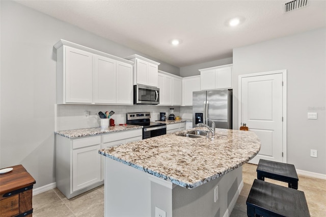 kitchen with sink, a center island with sink, stainless steel appliances, light stone countertops, and white cabinets