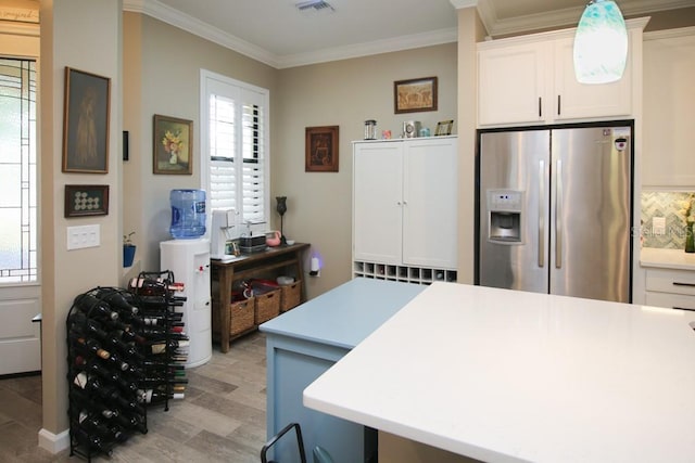 kitchen with white cabinetry, stainless steel fridge, crown molding, and a wealth of natural light