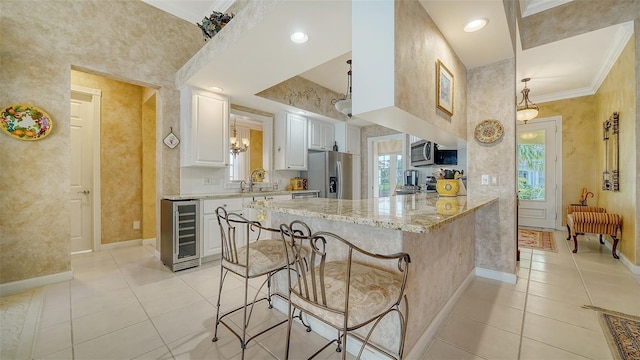 kitchen with white cabinetry, appliances with stainless steel finishes, a kitchen breakfast bar, kitchen peninsula, and beverage cooler