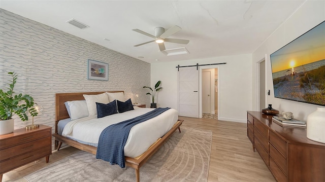 bedroom featuring ceiling fan, a barn door, and light wood-type flooring