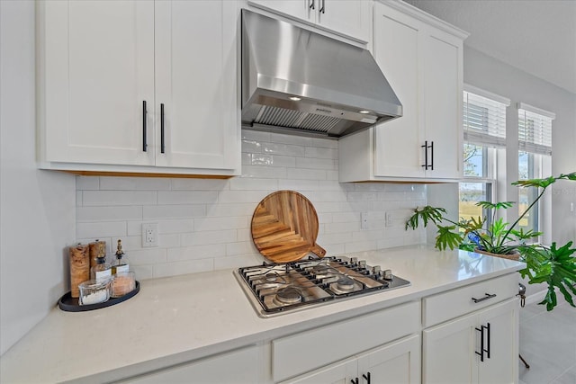 kitchen with light tile patterned flooring, stainless steel gas stovetop, white cabinetry, backsplash, and exhaust hood