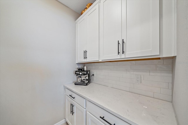 bar featuring light stone countertops, decorative backsplash, and white cabinets