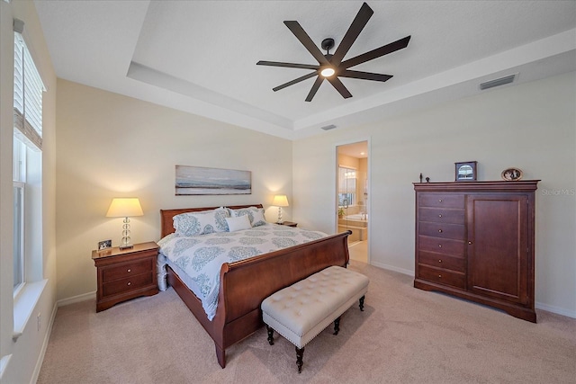 bedroom featuring ceiling fan, ensuite bath, a raised ceiling, and light colored carpet