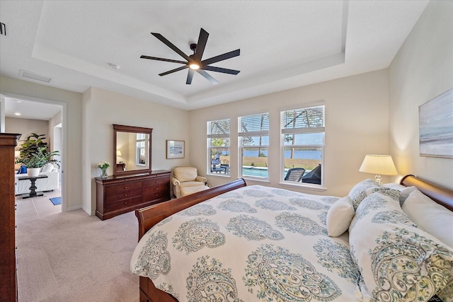 bedroom featuring a water view, light colored carpet, a raised ceiling, and ceiling fan