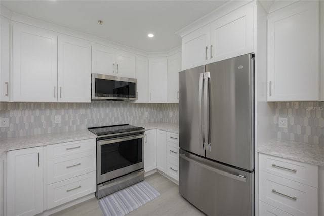 kitchen with appliances with stainless steel finishes, white cabinets, backsplash, light stone counters, and light hardwood / wood-style flooring