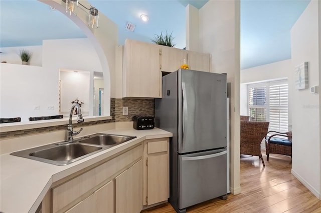 kitchen with sink, stainless steel fridge, tasteful backsplash, light brown cabinets, and light wood-type flooring