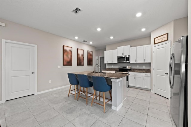 kitchen with visible vents, appliances with stainless steel finishes, a kitchen bar, white cabinetry, and a sink