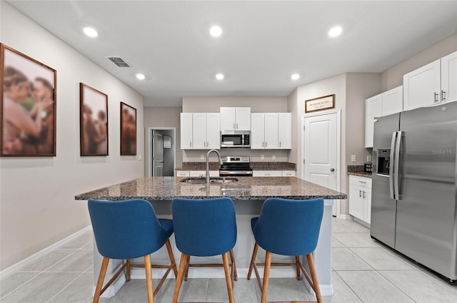 kitchen with light tile patterned floors, a sink, visible vents, appliances with stainless steel finishes, and dark stone countertops