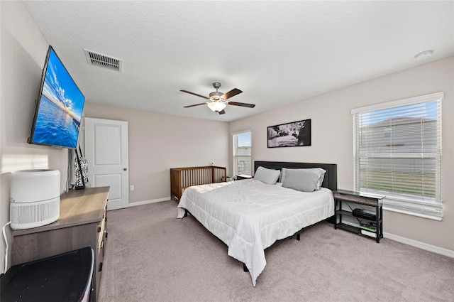 bedroom with visible vents, a ceiling fan, light carpet, a textured ceiling, and baseboards