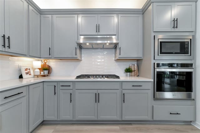 kitchen featuring exhaust hood, light countertops, appliances with stainless steel finishes, gray cabinets, and decorative backsplash