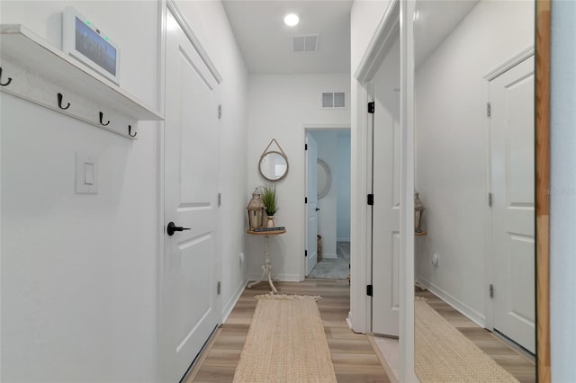 hallway with baseboards, visible vents, and light wood finished floors