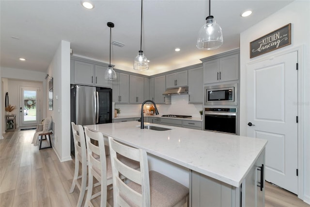 kitchen featuring under cabinet range hood, stainless steel appliances, a sink, and gray cabinetry