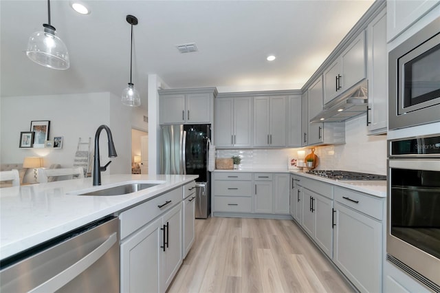 kitchen with gray cabinetry, under cabinet range hood, stainless steel appliances, a sink, and visible vents