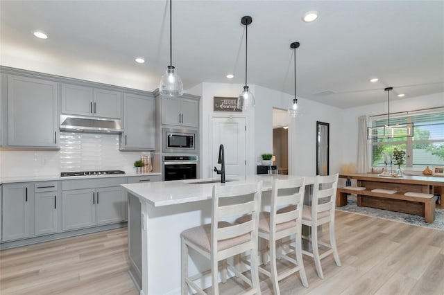 kitchen featuring under cabinet range hood, gray cabinetry, a sink, light countertops, and appliances with stainless steel finishes