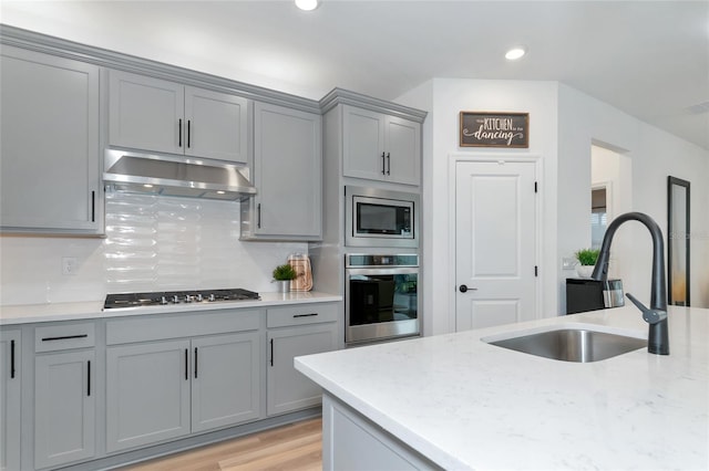 kitchen featuring a sink, stainless steel appliances, gray cabinetry, under cabinet range hood, and backsplash