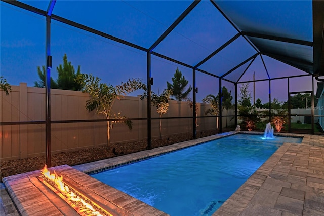 pool at dusk with a fire pit, glass enclosure, and a fenced backyard