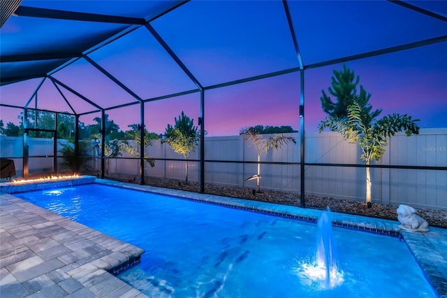 pool at dusk featuring glass enclosure and a fenced backyard