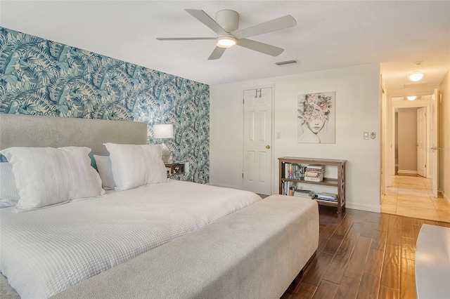 bedroom featuring an accent wall, wood finished floors, visible vents, baseboards, and wallpapered walls