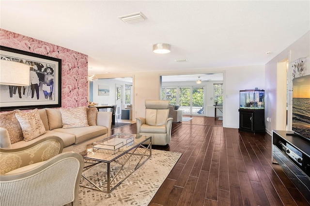 living room with an accent wall, dark wood-style flooring, visible vents, and wallpapered walls