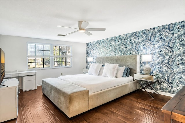 bedroom featuring dark wood finished floors, an accent wall, a ceiling fan, baseboards, and wallpapered walls