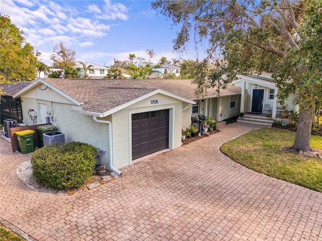 ranch-style home featuring decorative driveway, stucco siding, a shingled roof, central AC, and a garage