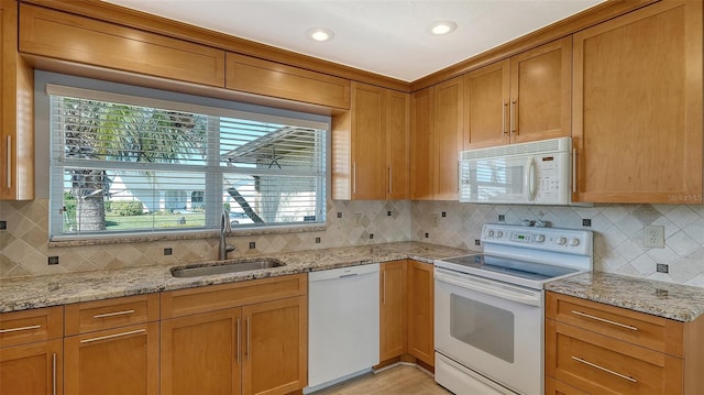 kitchen featuring light stone counters, sink, white appliances, and decorative backsplash